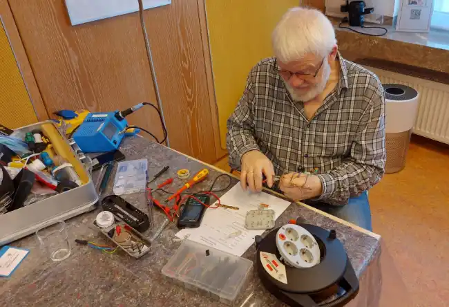 Ein Mann repariert an einem Tisch elektrische Geräte im Repaircafé.